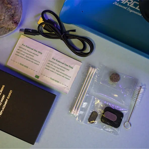 This photo shows the AirVape Legacy Pro's accessories spread across a table top. Some of the accessories are wrapped in plastic, and they all came out of a small cardboard box in the kit.
